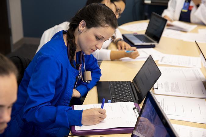 Current Students - A group of people sitting at a table using a laptop computer - Education